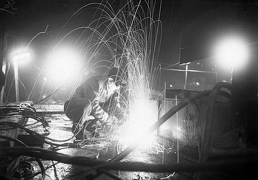 A burner in operation on the deck of a ship at night at Harland and Wolff's yard