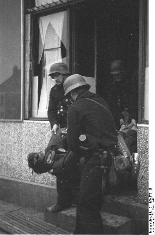 Three German Marines carrying a fallen British soldier from a house,